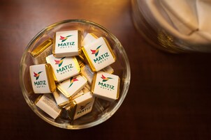 Un tazón de vidrio lleno de pequeñas cajas blancas y doradas con la etiqueta 'MATIZ HOTEL'.