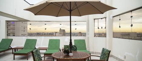 Una terraza en la azotea con una mesa, sillas, un paraguas grande y vistas al horizonte de la ciudad.