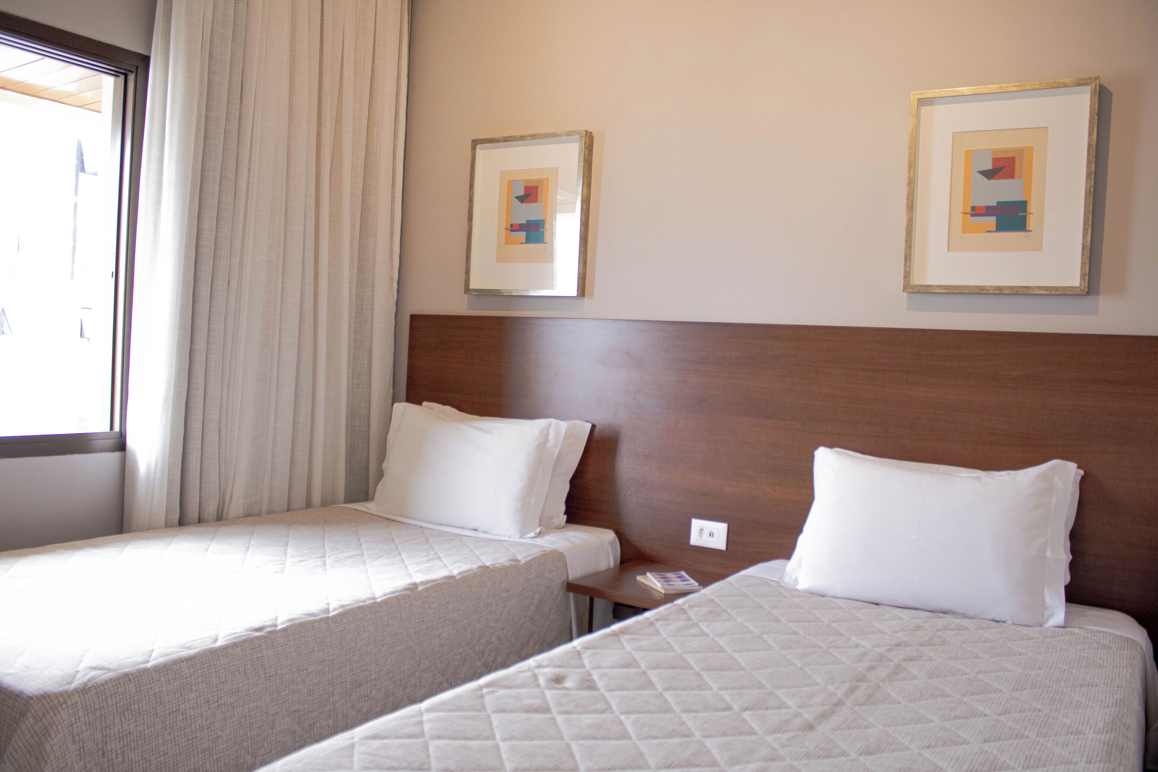 A hotel room with two beds, a wooden headboard, and two framed artworks on the wall.