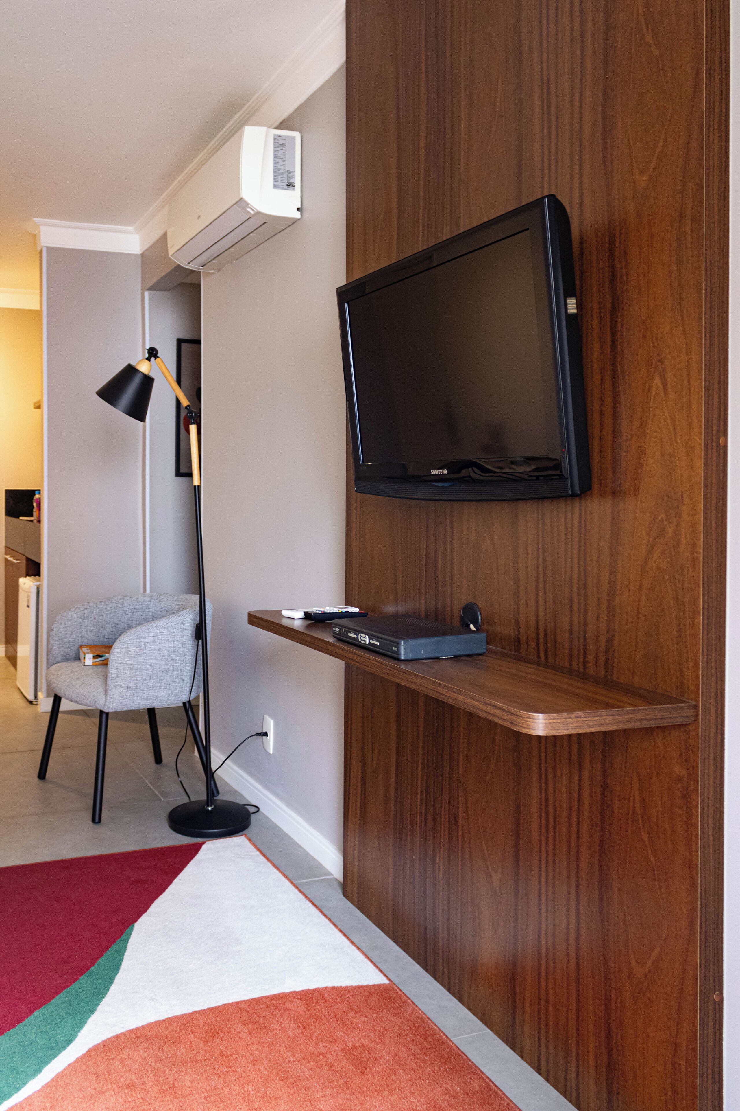 A modern living room with a mounted TV, a standing lamp, a bookshelf, and a colorful rug.