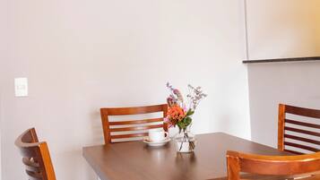 A dining area with a wooden table and four chairs, a vase with flowers, and a light switch on the wall.