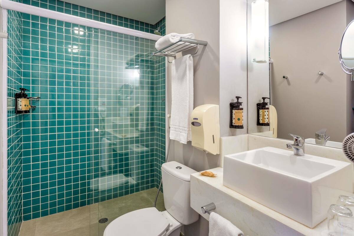 A bathroom with a shower, toilet, sink, and a mirror.