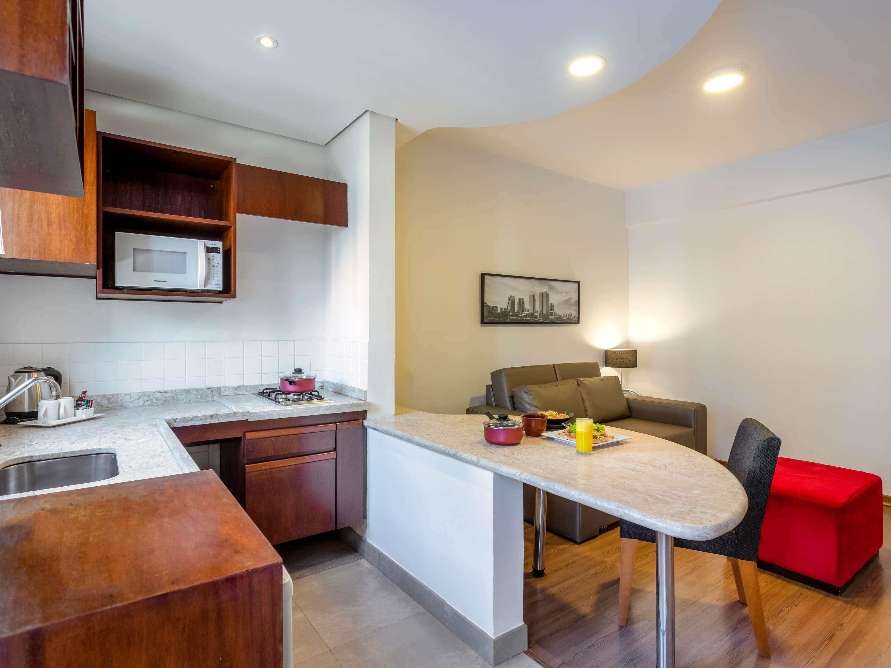 A compact kitchen with a microwave, stove, and sink, a dining area with a table and chairs, and a sofa.