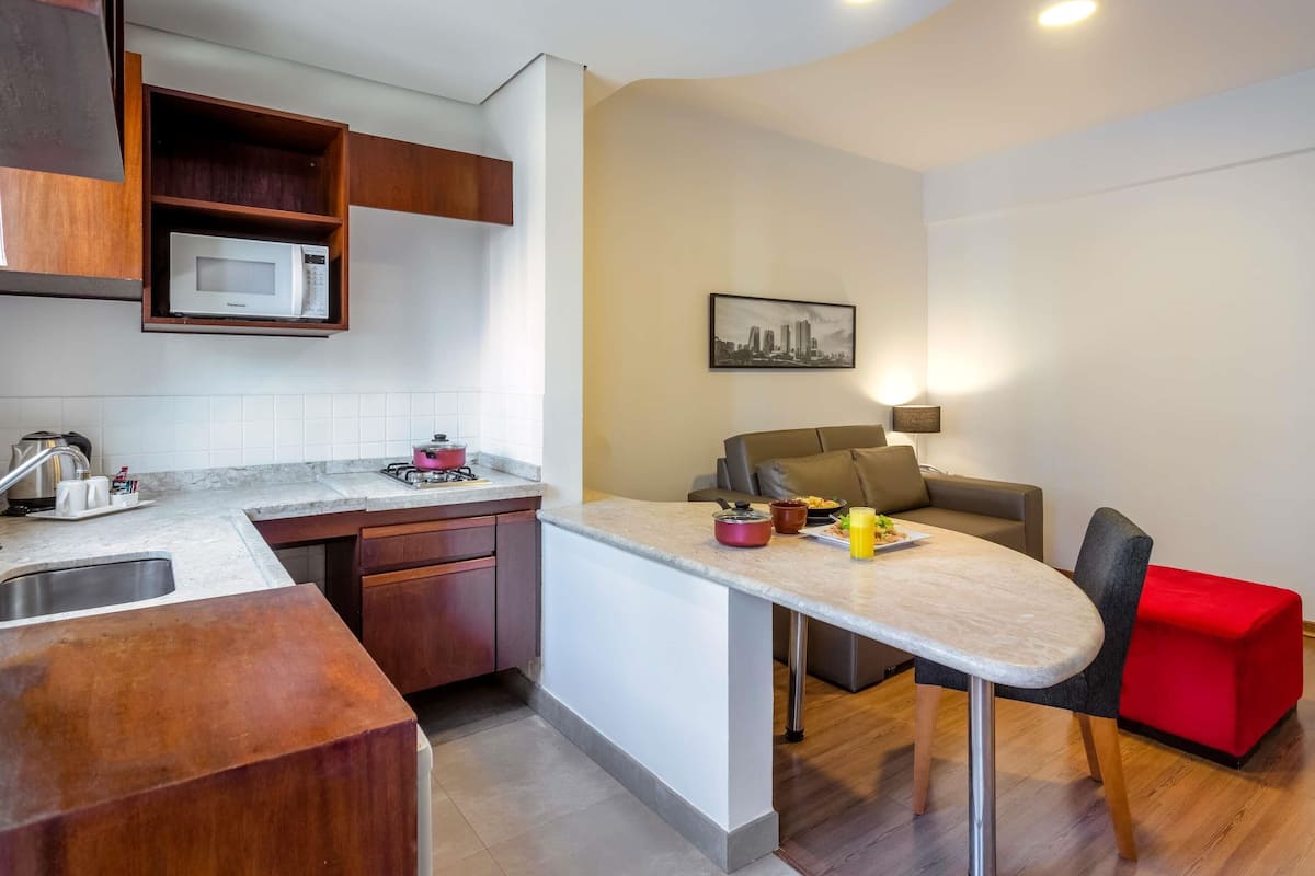 A compact kitchen with a microwave, stove, and sink, a dining area with a table and chairs, and a sofa.