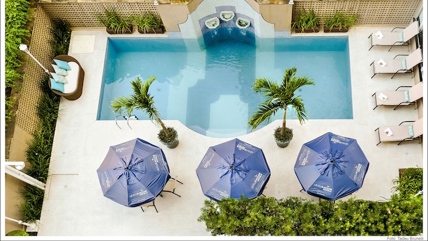 A swimming pool with lounge chairs and umbrellas, surrounded by greenery. - Mercure São Paulo JK (São Paulo)