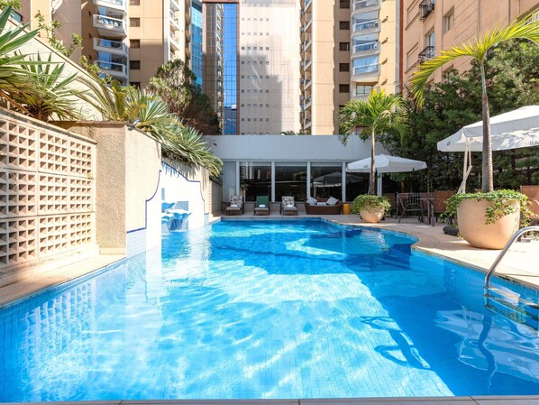 Una piscina al aire libre, sombrillas, sillones reclinables de piscina