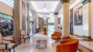 A spacious lobby with high ceilings, large columns, and a chandelier. There are seating areas with chairs and tables, and a large window with curtains. - Mercure São Paulo JK (São Paulo)