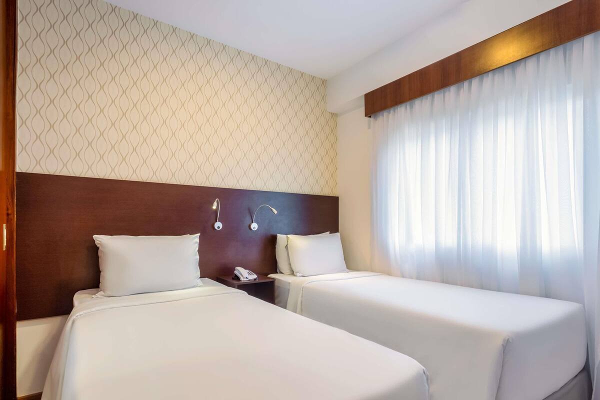 A hotel room with two beds, a wooden headboard, a telephone, and a patterned wall.