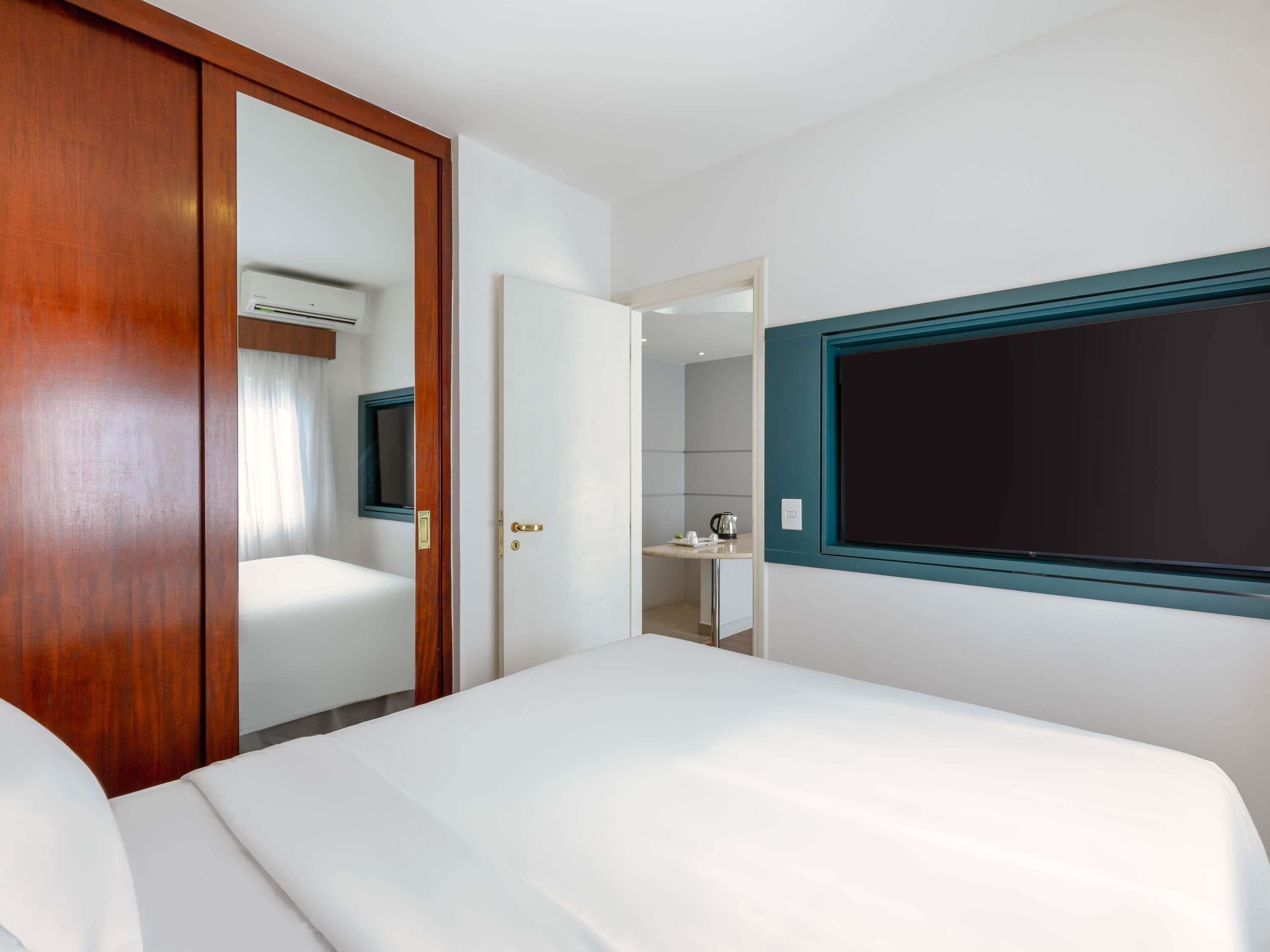A hotel room with a bed, a wardrobe, a mirror, and a wall-mounted TV.