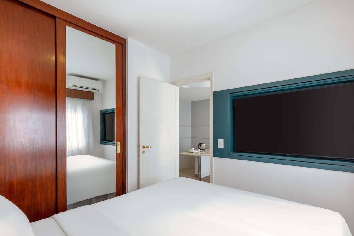 A hotel room with a bed, a wardrobe, a mirror, and a wall-mounted TV.