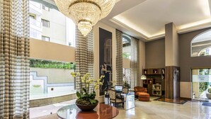 A spacious lobby with a large chandelier, a round table with a bowl of flowers, and a seating area with a sofa and chairs. - Mercure São Paulo JK (São Paulo)