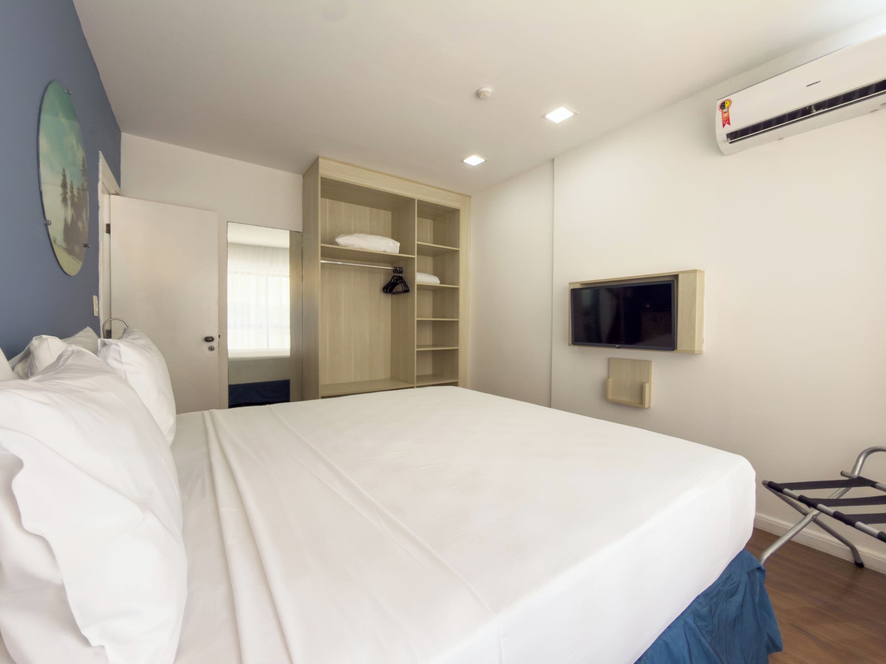 Una habitación de hotel con cama, armario, televisor y aire acondicionado.