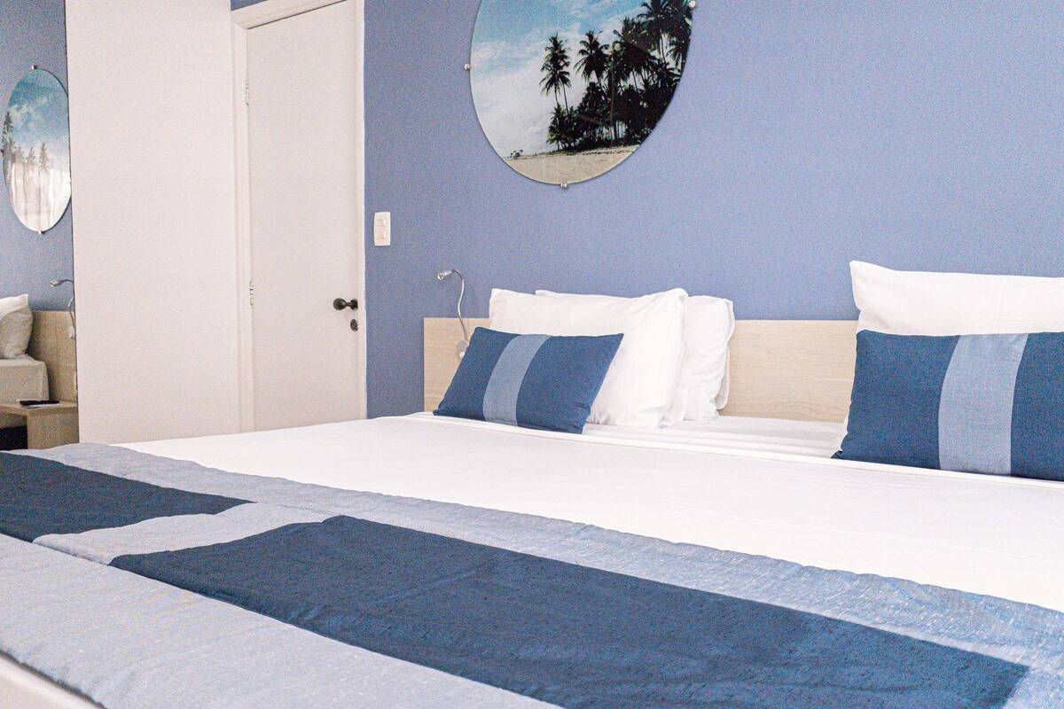 Ein Bett mit blauer und weißer Bettdecke, ein runder Wandspiegel und eine Tür.