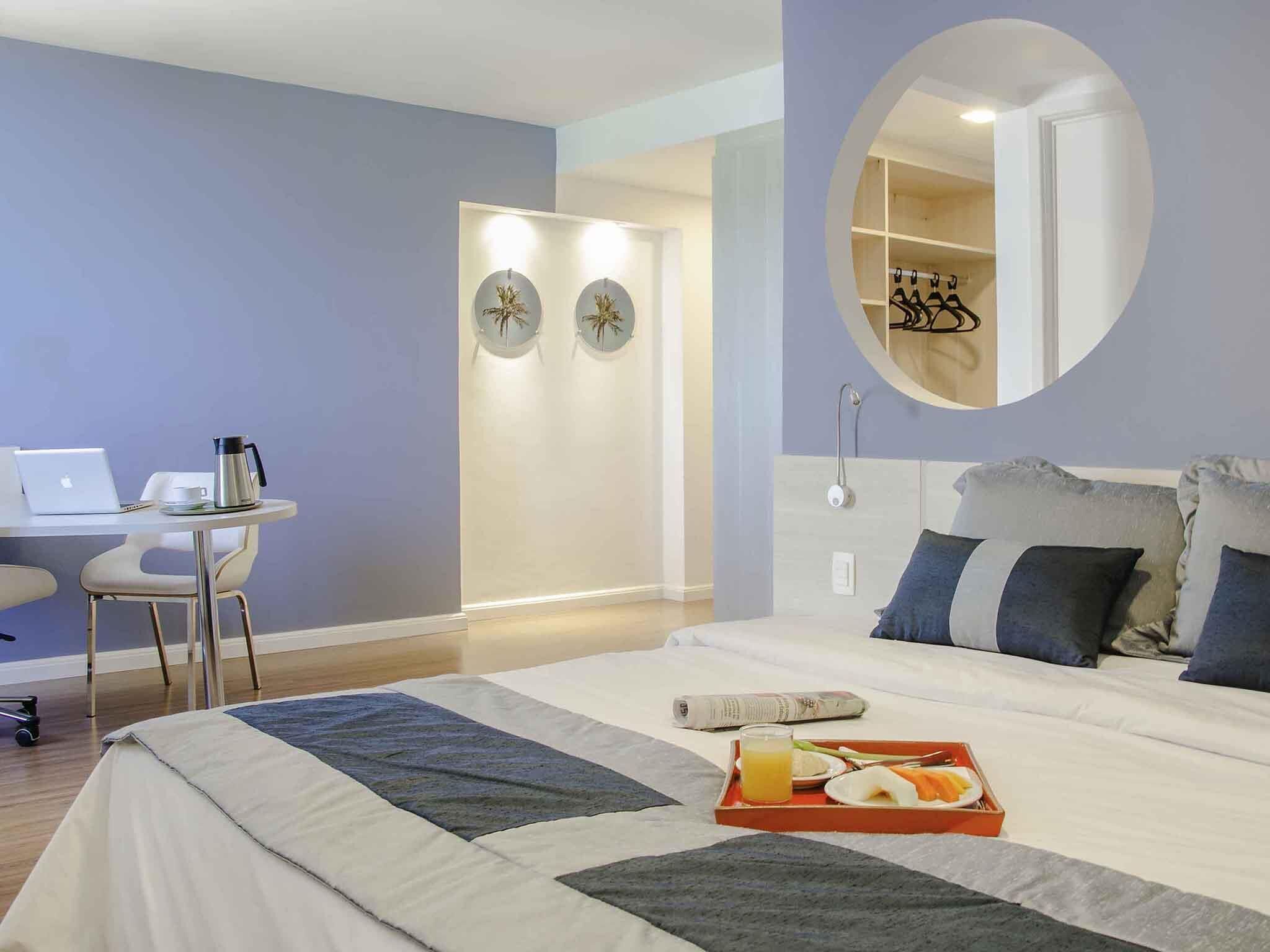 A hotel room with a bed, a desk, a chair, a laptop, a coffee maker, and a breakfast tray.