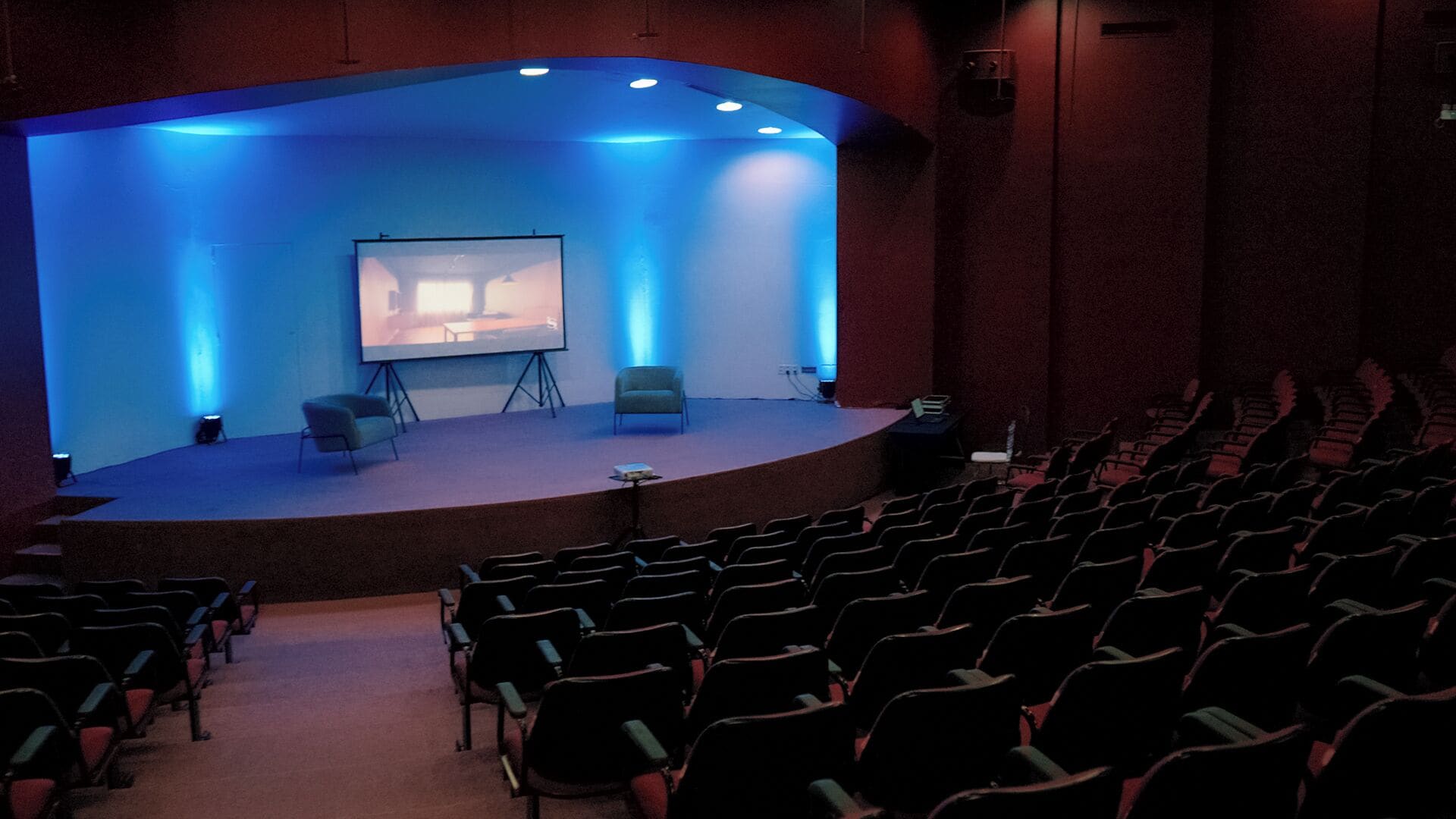 Un auditorium con un palco, sedie e uno schermo.
