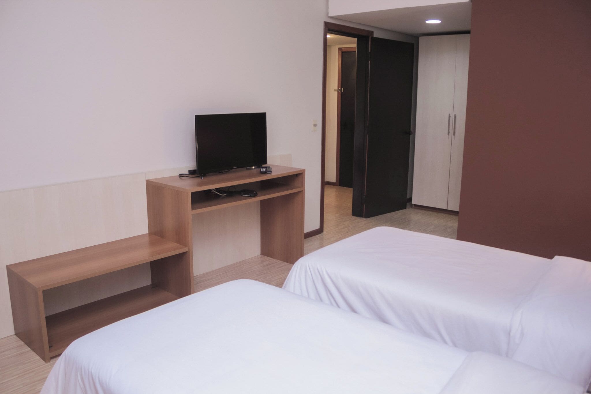 A hotel room with two beds, a TV on a wooden stand, and a wardrobe.