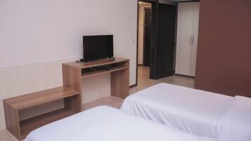 A hotel room with two beds, a TV on a wooden stand, and a wardrobe.