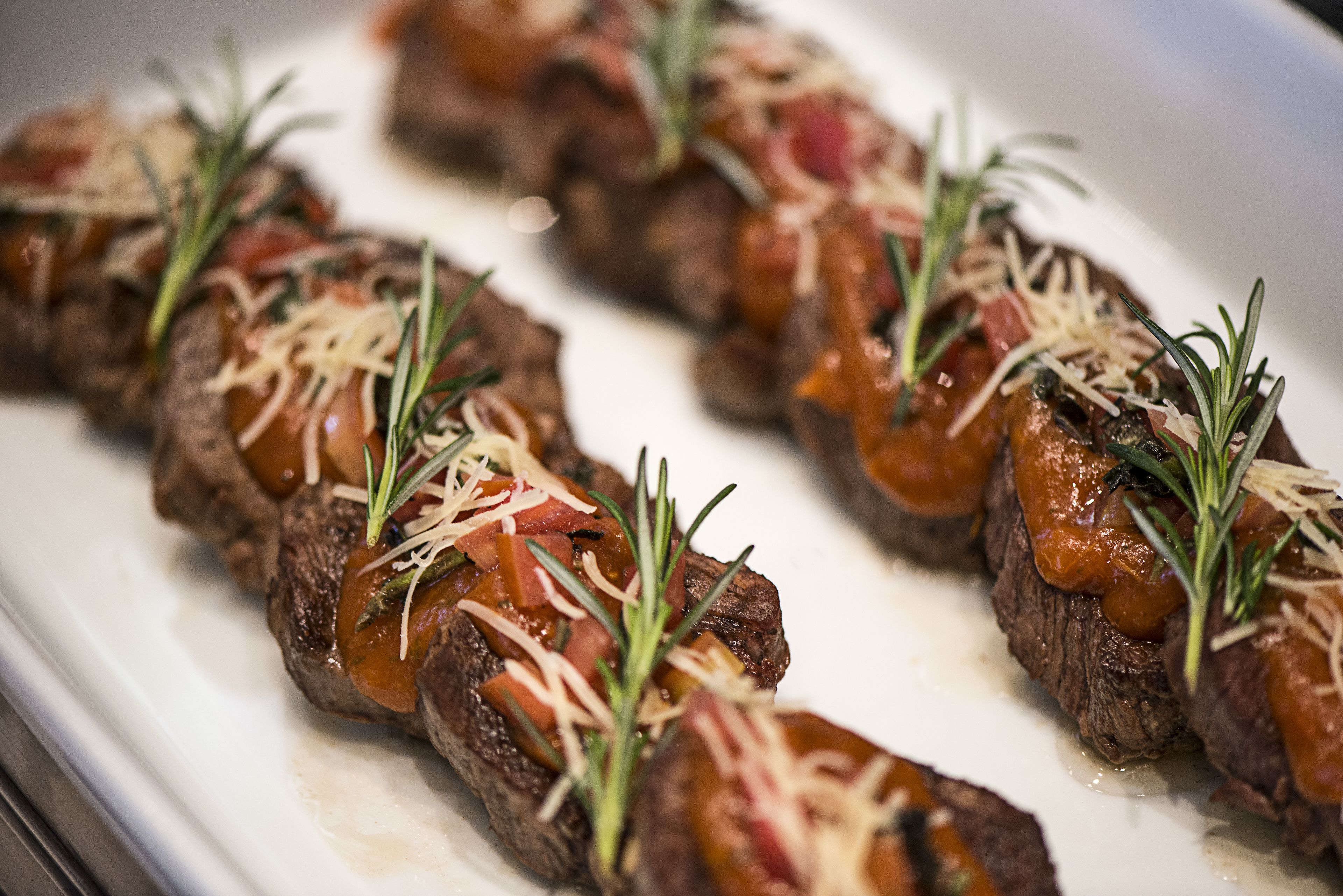 A close-up of a dish with sliced meat, tomatoes, cheese, and herbs.