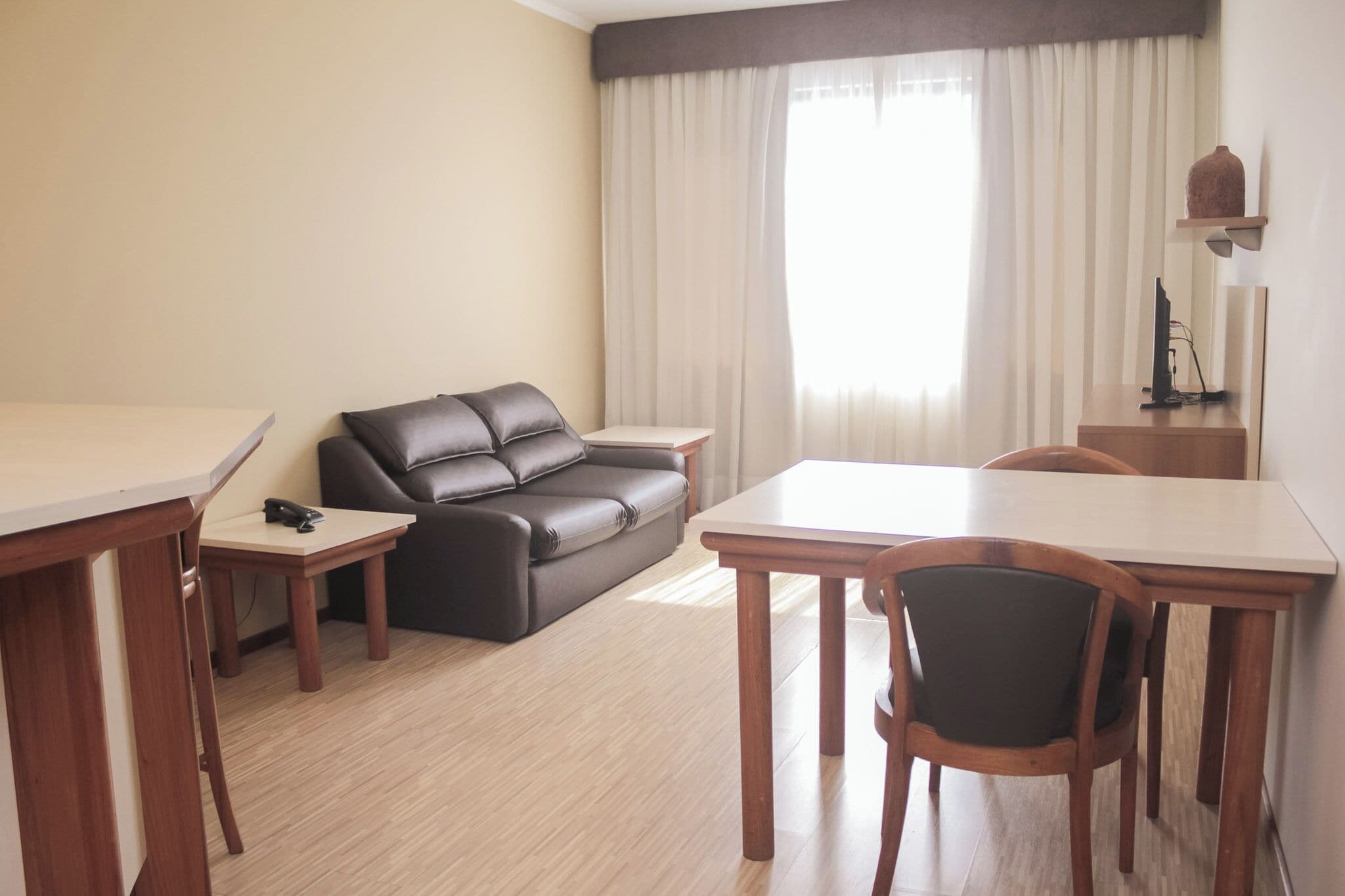 Uma sala compacta com um sofá, uma mesa de jantar e uma TV sobre um suporte.