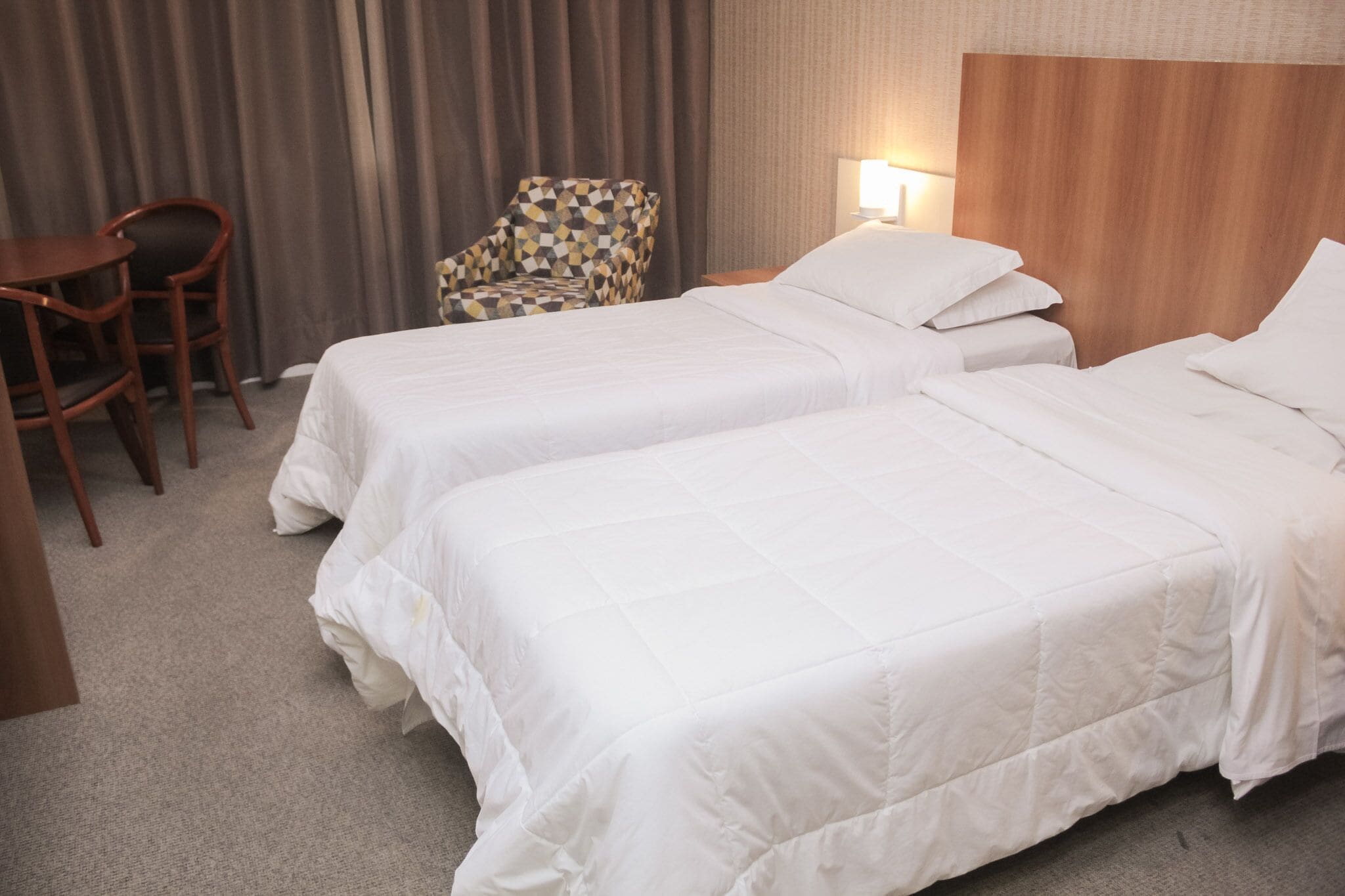 Habitación de hotel con dos camas, cabecero de madera, escritorio, silla y lámpara.