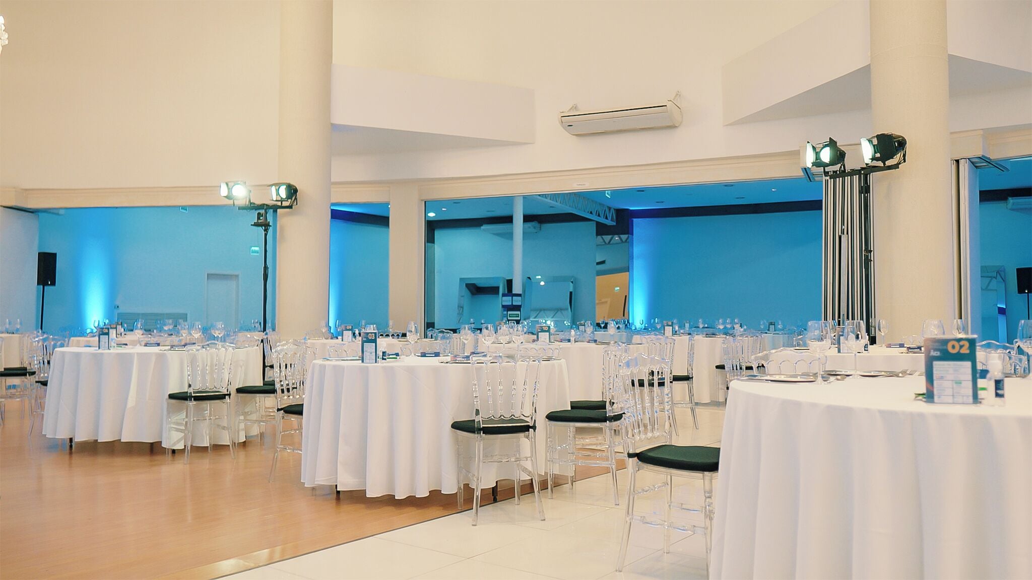 Un amplio salón de banquetes con mesas redondas, sillas transparentes e iluminación azul.