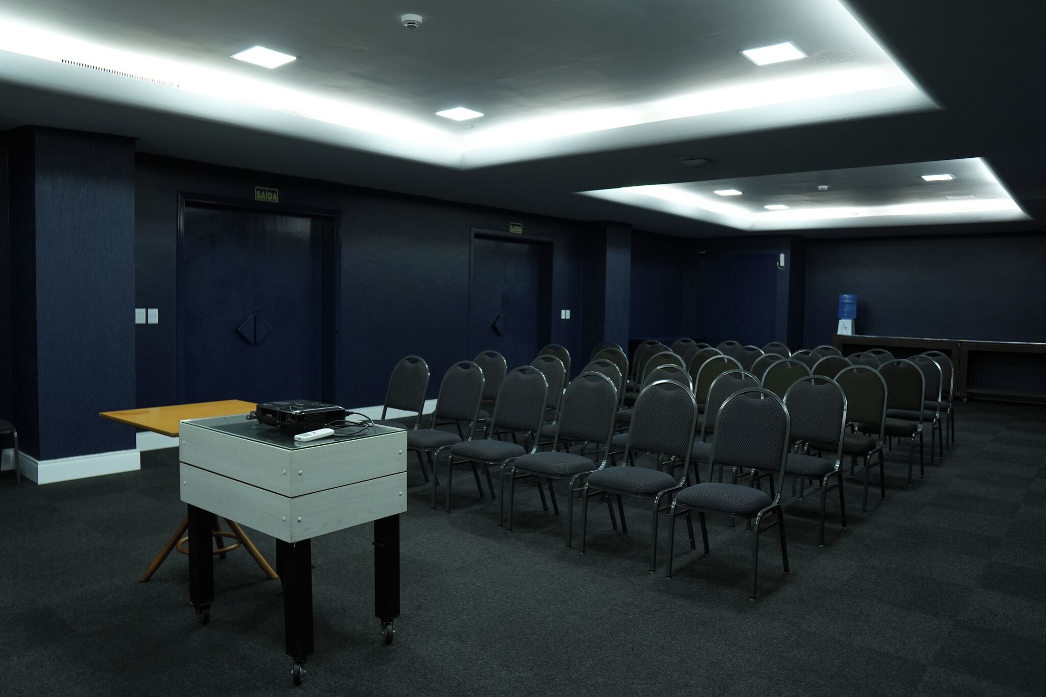 A conference room with rows of chairs, a table with a laptop, and a water dispenser.
