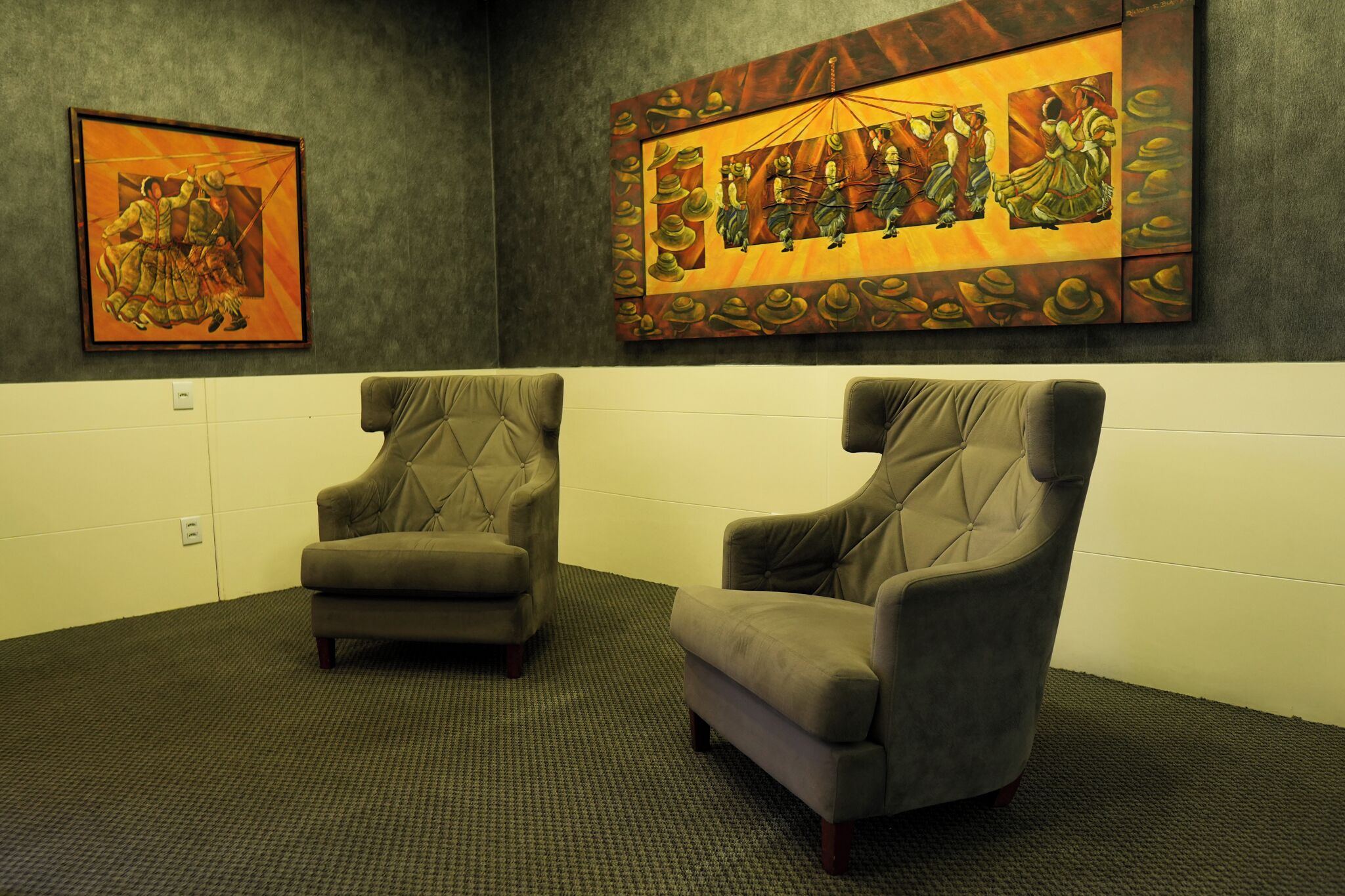 Um quarto com duas poltronas cinzentas, um quadro grande na parede e piso coberto de carpete.