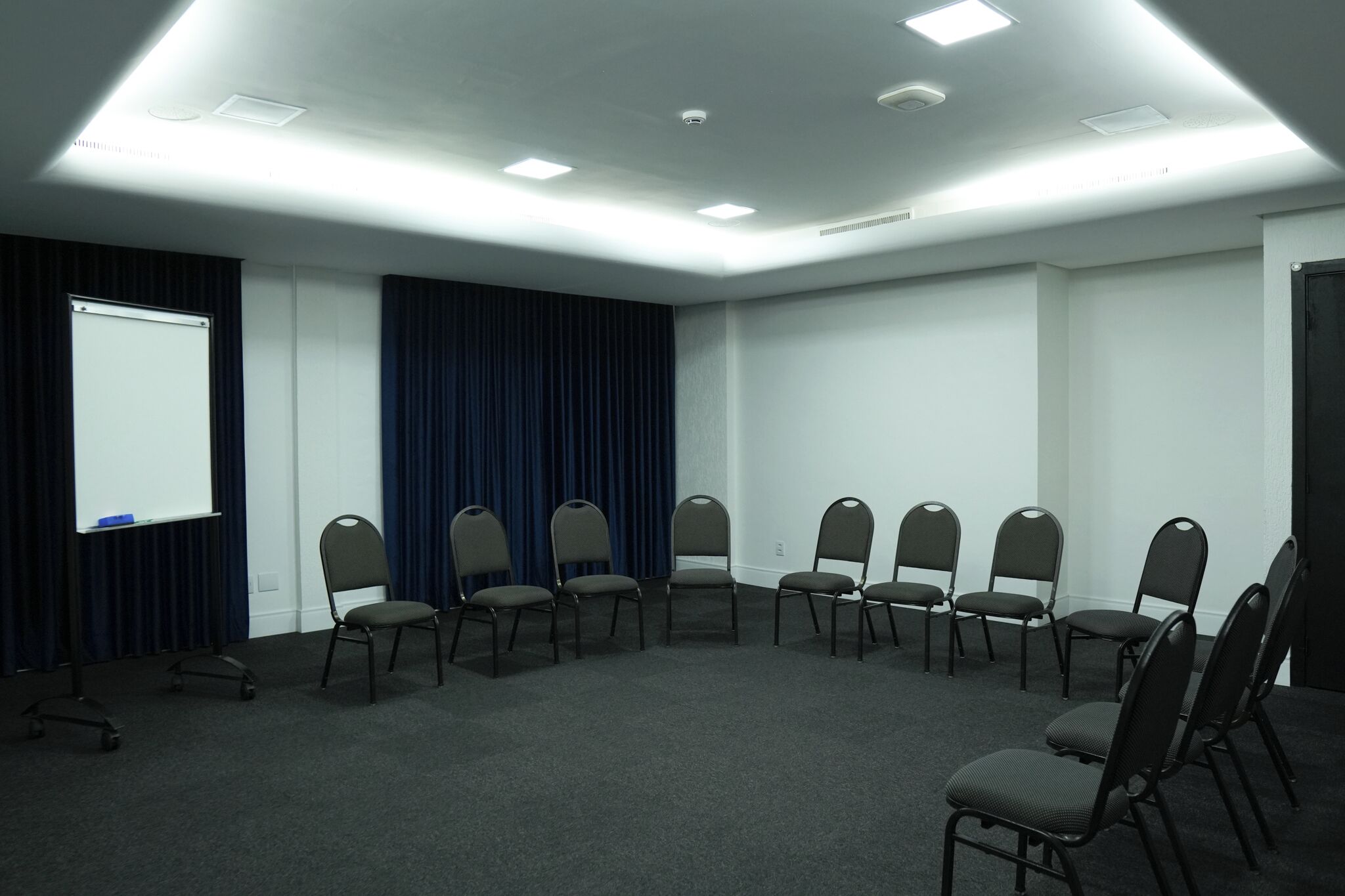 Ein Konferenzraum mit einer Whiteboard-Tafel, dunklen Vorhängen und einer Reihe von Stühlen.