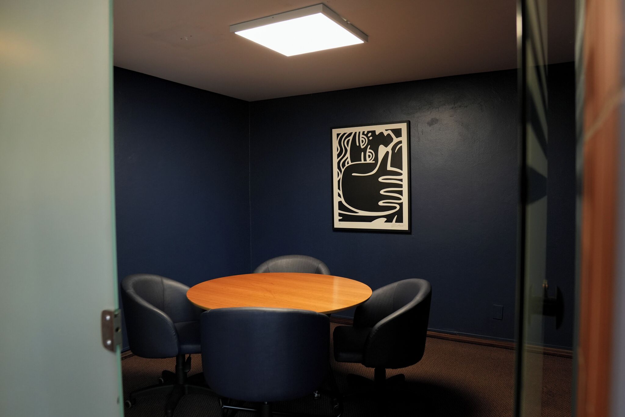 Une salle de conférence équipée d’une table ronde, de quatre chaises, d’une œuvre d’art abstraite accrochée au mur et d’un luminaire au plafond.