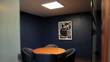 Une salle de conférence équipée d’une table ronde, de quatre chaises, d’une œuvre d’art abstraite accrochée au mur et d’un luminaire au plafond.