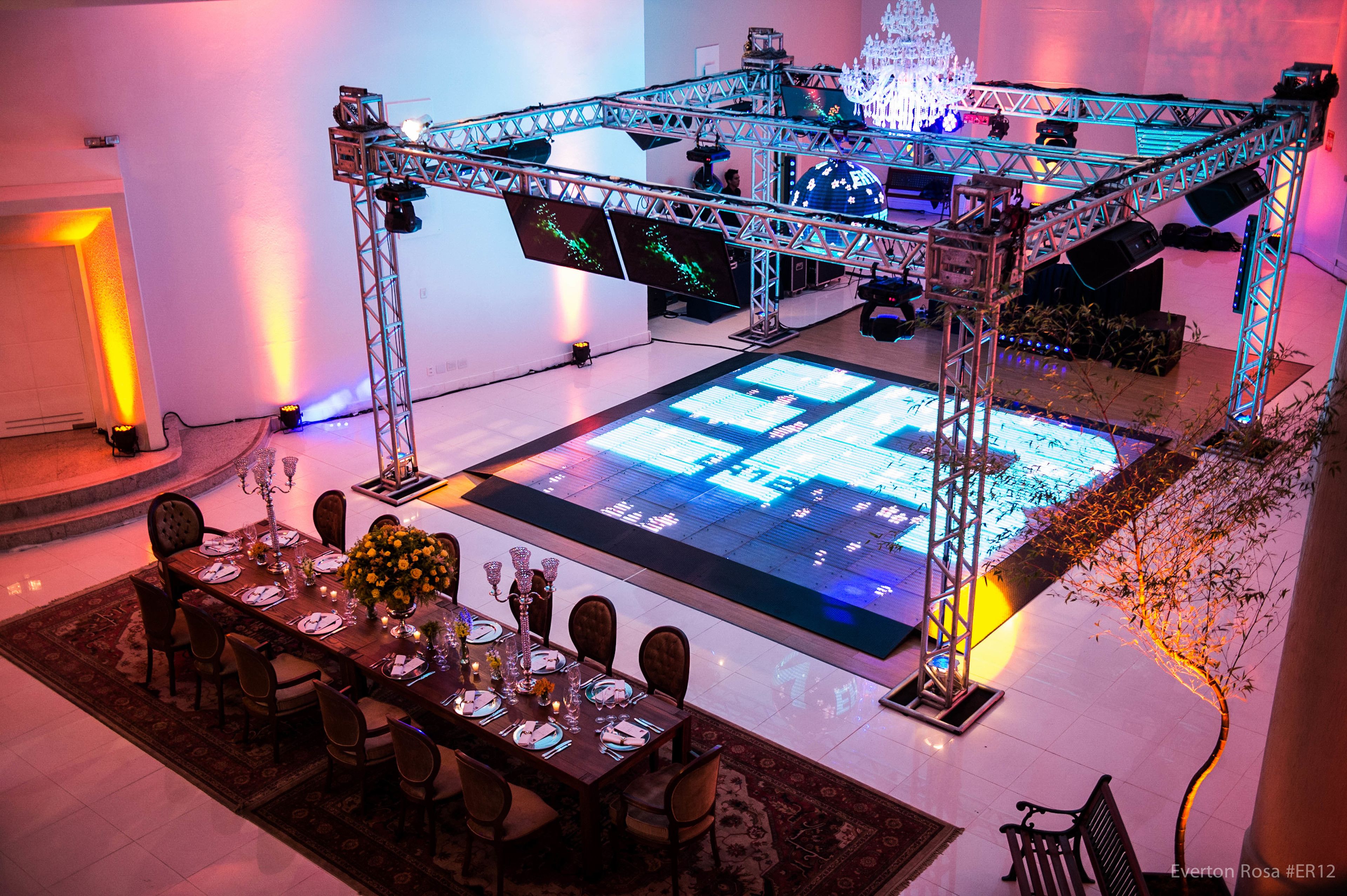 A dining area with a large table set for a meal, a stage with lighting equipment, and a chandelier.