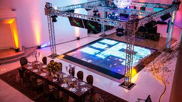 A dining area with a large table set for a meal, a stage with lighting equipment, and a chandelier.