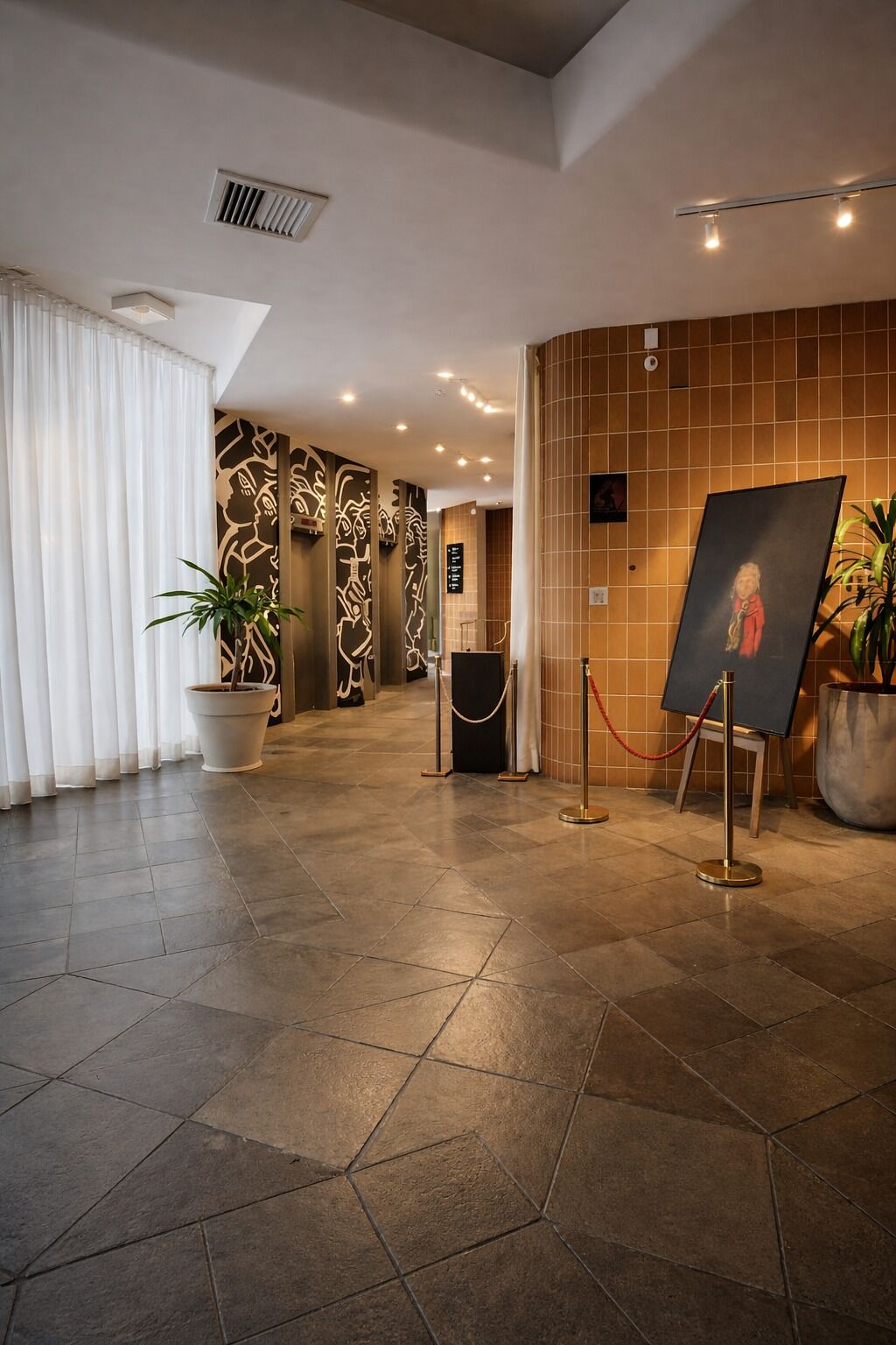 A lobby with a tiled floor, a potted plant, a painting on easels, and a wall with a geometric pattern.