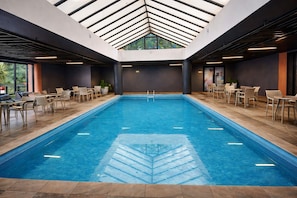 An indoor swimming pool with a geometric ceiling design, surrounded by seating areas. - Swan Novo Hamburgo (Novo Hamburgo)