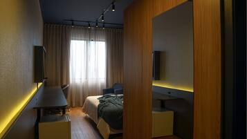 Quarto de hotel moderno com uma cama, escrivaninha, cadeira e um espelho grande.