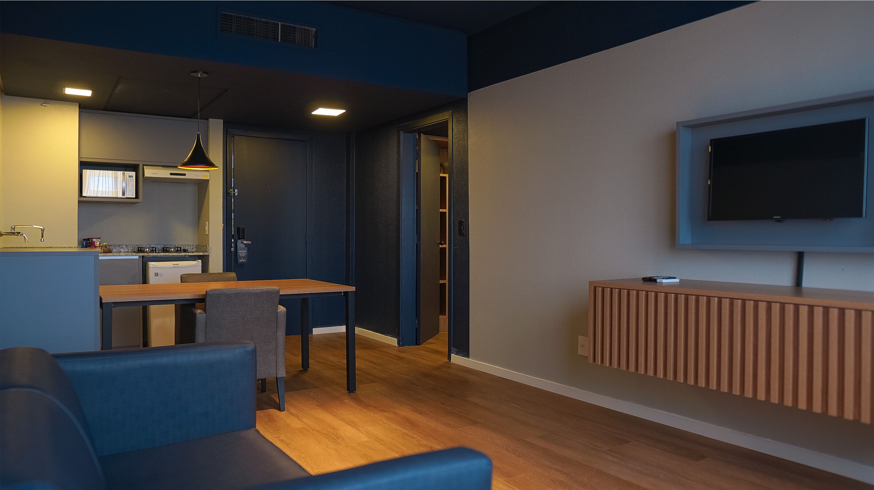 A modern living room with a dining area, a kitchen, and a TV mounted on the wall.