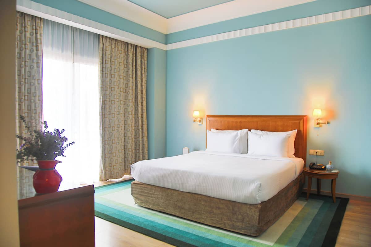 A hotel room with a large bed, two bedside lamps, a small table, and a vase with flowers.