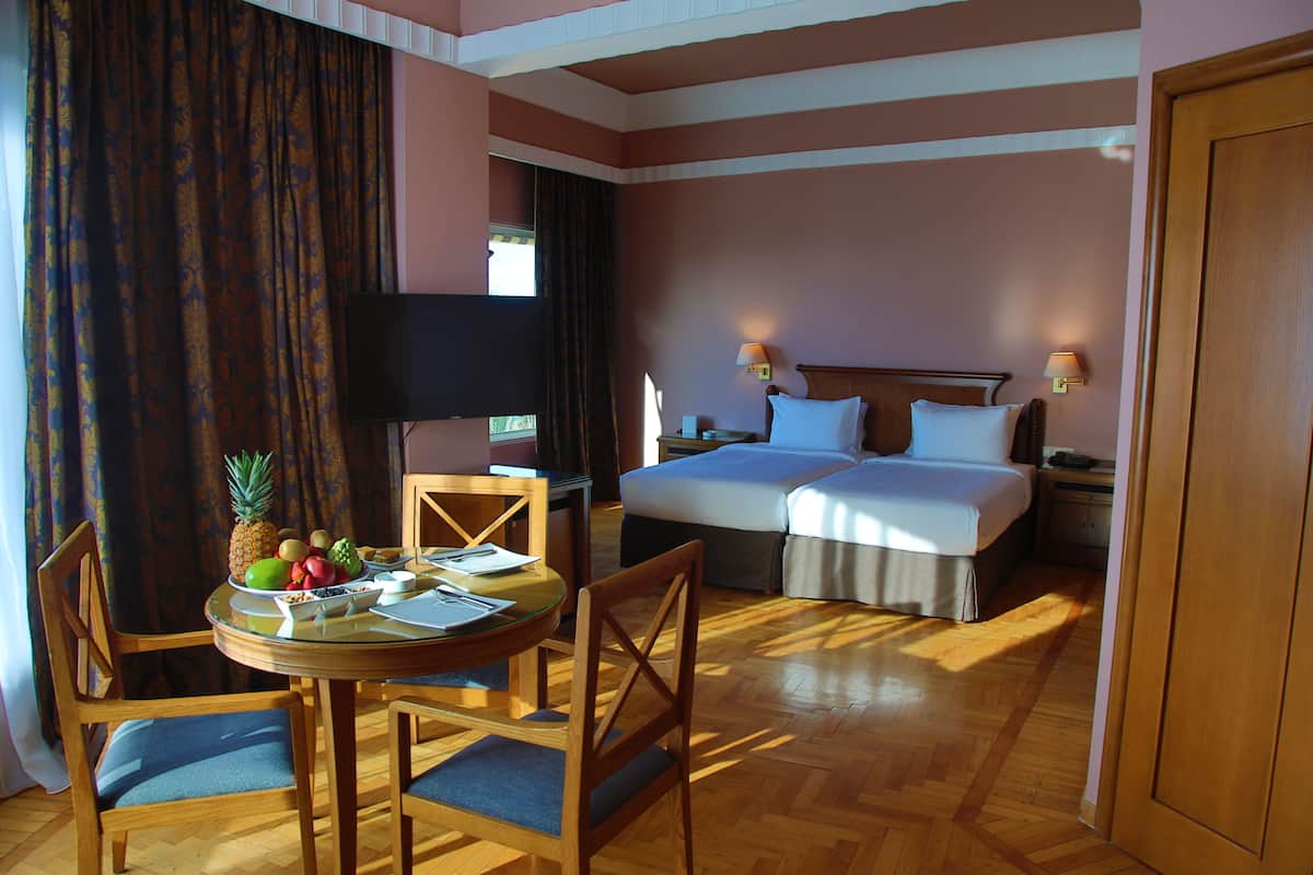 A hotel room with a bed, two bedside tables, a TV, a dining table with chairs, and a fruit bowl.