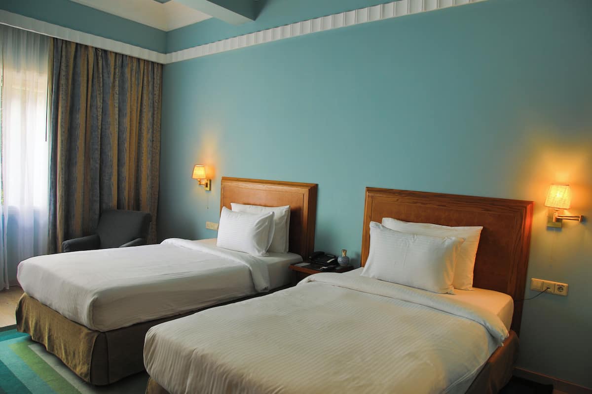 A hotel room with two beds, a chair, a lamp, and a nightstand.