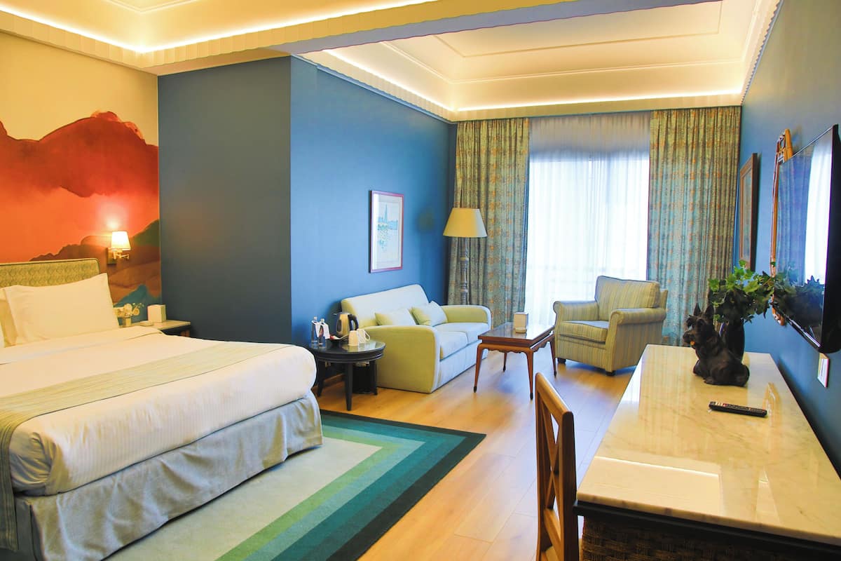A hotel room with a bed, a sofa, a dining table, a lamp, and a television.