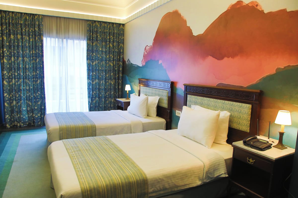 A hotel room with two beds, a nightstand with a phone, a lamp, and a wall mural.