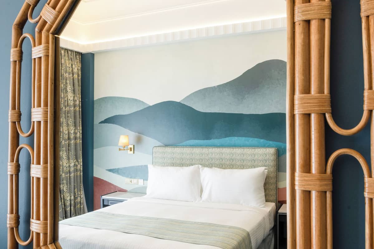 A room with a large octagonal mirror, a bed with a headboard, a nightstand, and a wall-mounted lamp.