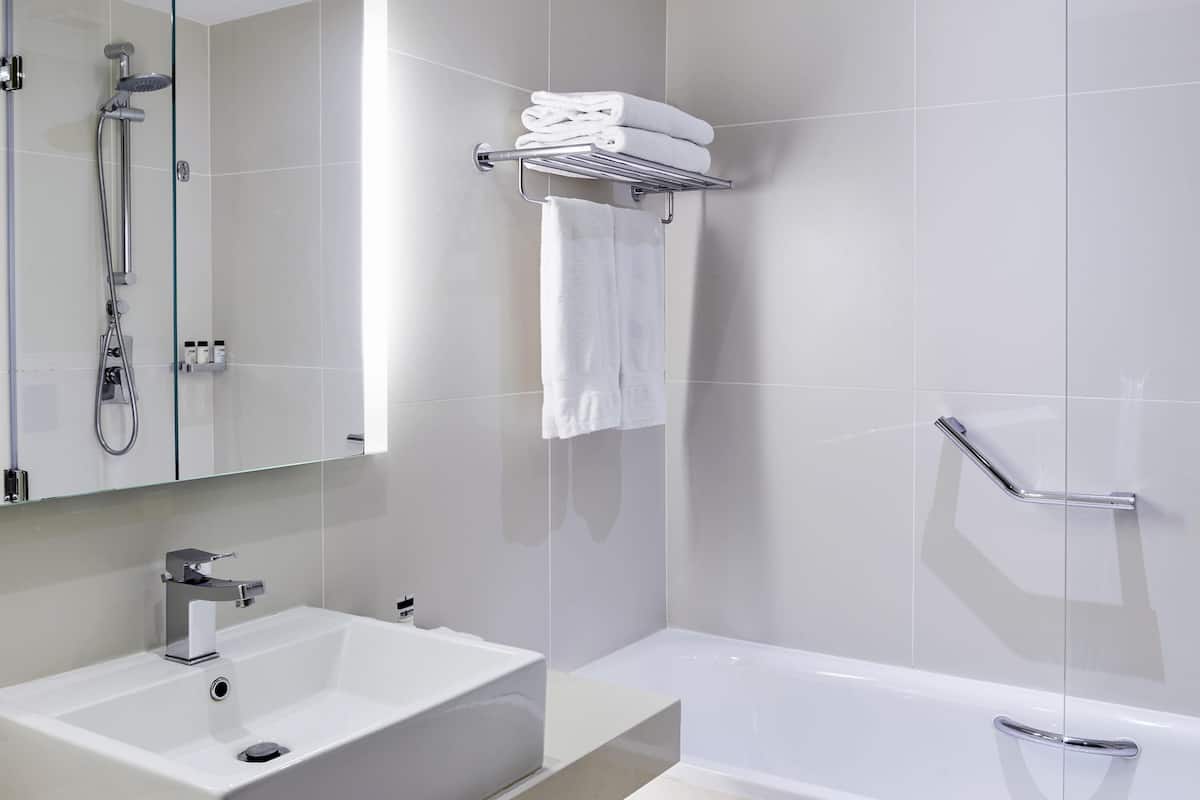 A modern bathroom with a white sink, a bathtub, a glass shower enclosure, and a towel rack.