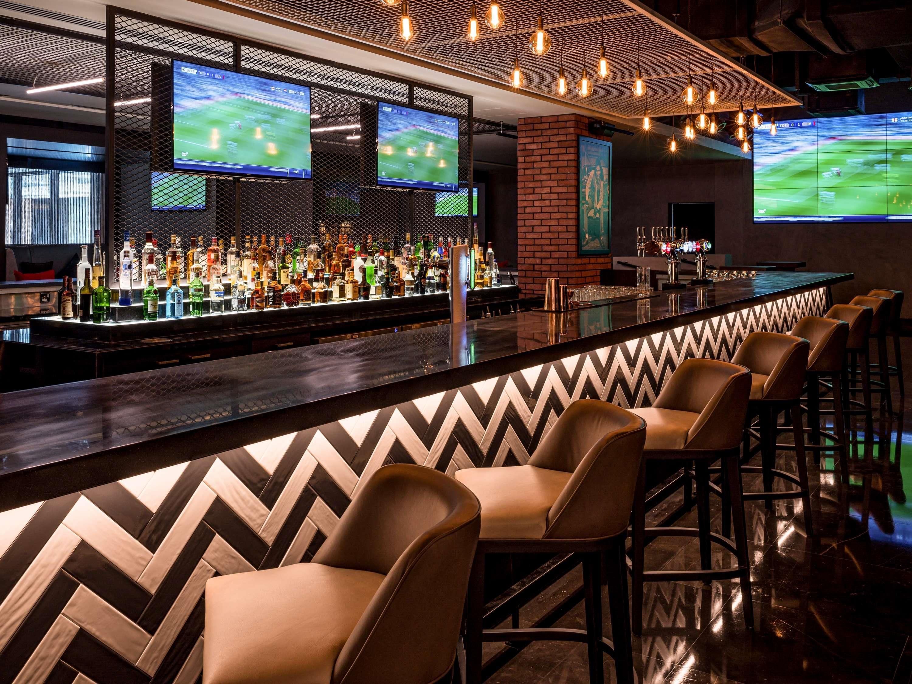A bar area with multiple screens displaying sports, a variety of liquor bottles, and leather bar stools.