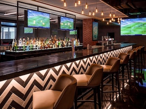 A bar area with multiple screens displaying sports, a variety of liquor bottles, and leather bar stools. - Pullman Dubai Creek City Centre (Dubai)