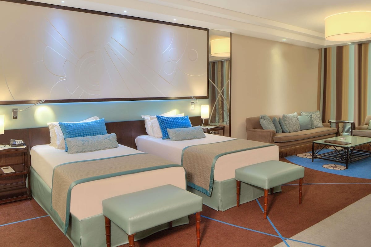 Habitación de hotel con dos camas, un sofá, una mesa de centro y un espejo grande.