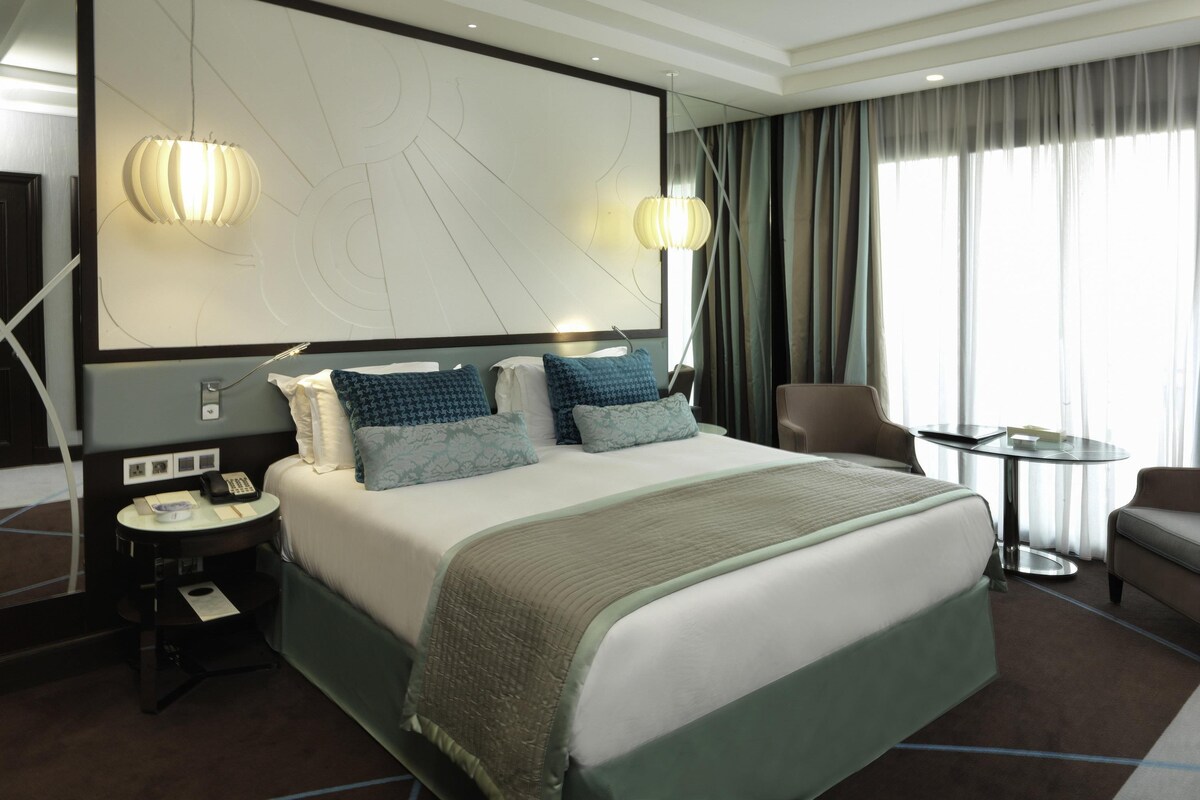 Une chambre d’hôtel avec un grand lit, des tables de chevet, un bureau, une chaise, un miroir et une vue sur l’extérieur.
