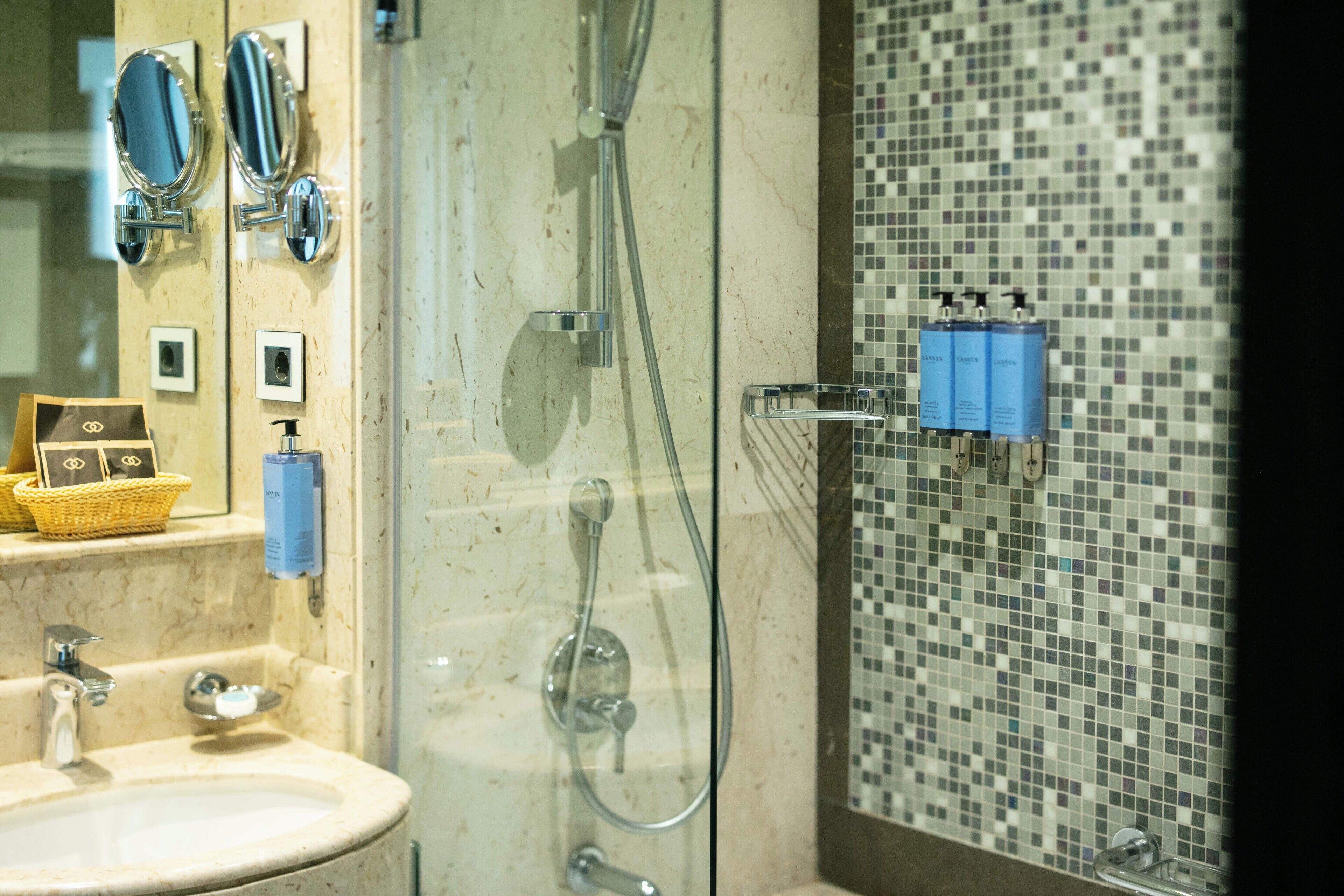 Un baño con lavamanos, espejos, ducha y pared con azulejos.