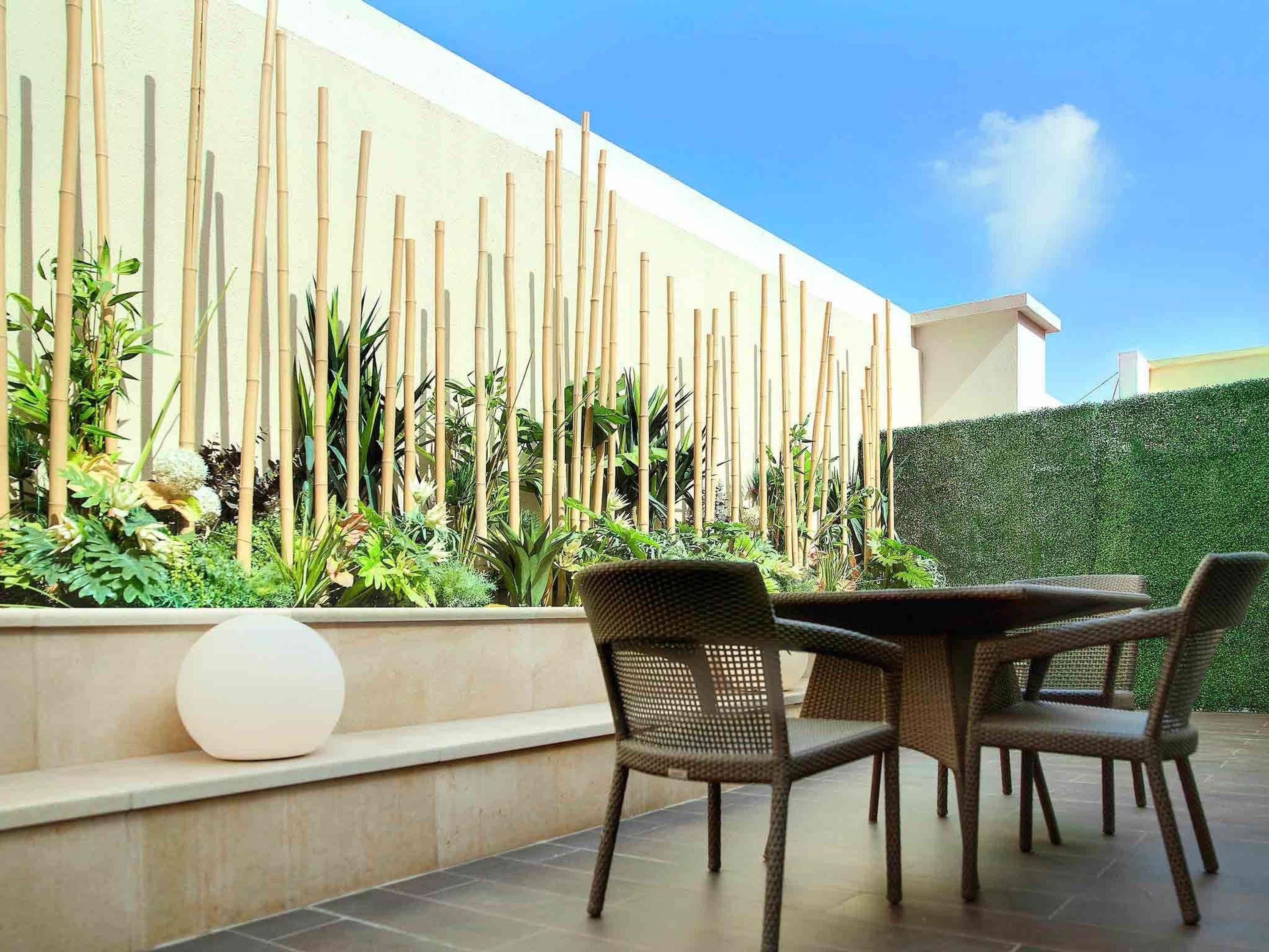 Patio esterno con tavolo rotondo e sedie in vimini, circondato da piante di bambù e vario verde.