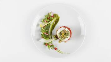 A white plate with a salad, a dollop of sauce, and a small round item.